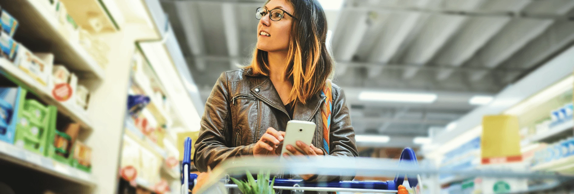 Woman using her phone and pushing a shopping cart with groceries